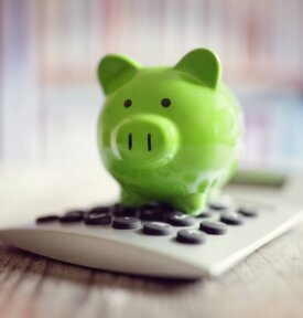 Green piggy bank standing on a calculator.