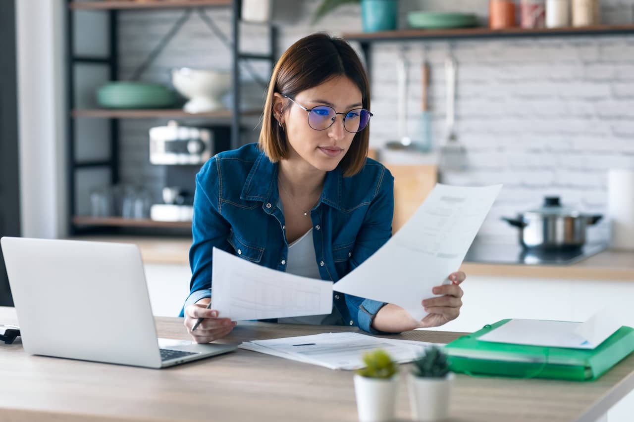 Small business owner examining invoices while using a laptop.